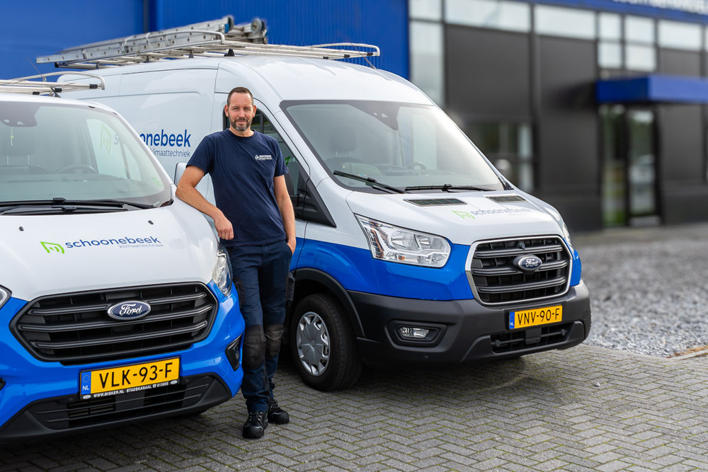 Monteur van Schoonebeek Klimaattechniek leunend tegen een bedrijfsbus