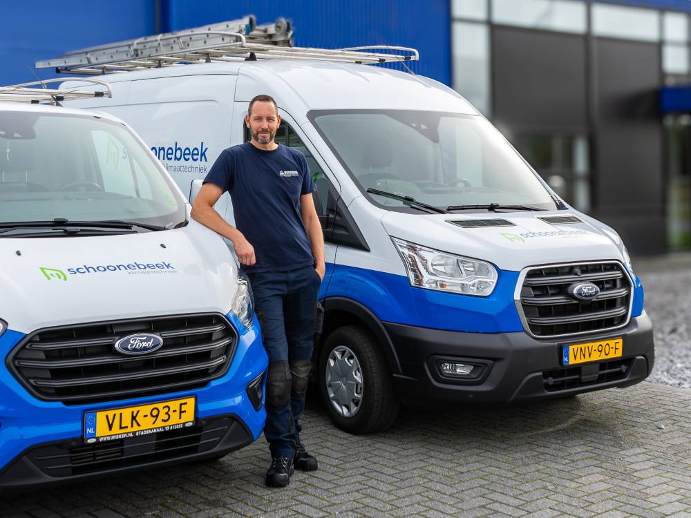 Monteur van Schoonebeek Klimaattechniek leunend tegen een bedrijfsbusje, klaar voor installatie.